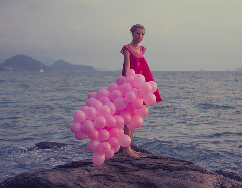 Young woman walking with big bunch o balloons in sunset