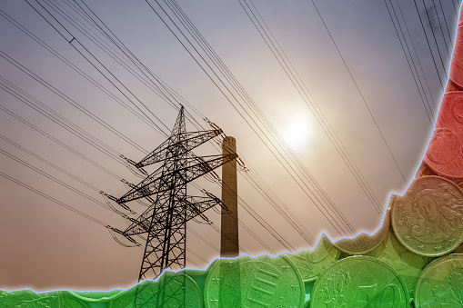 High voltage pylon and industrial chimney at sunset. A line diagram with a color gradient from green to red and coins as a symbol for exploding energy costs.
