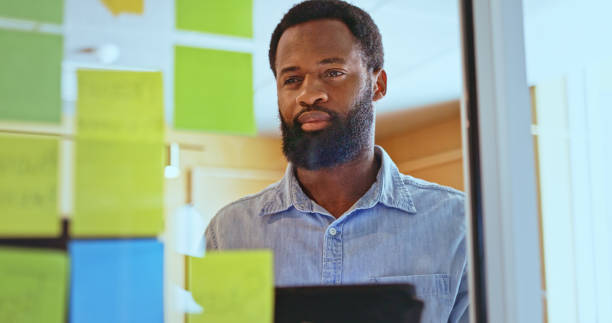 istock Bearded businessman reading sticky notes on glass wall in office 1886858551