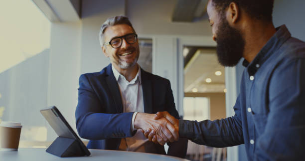 istock Multiracial business partners shaking hands cheerfully in office breakout space 1886858633