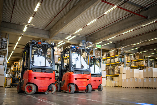 Red forklift vehicles for boxes transportation in empty warehouse with no people indoors, wide shot