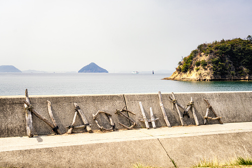 Naoshima Island, Japan - The word Naoshima spelled out in driftwood on a sea wall on the island, with a view of the sea and landscape in the distance.