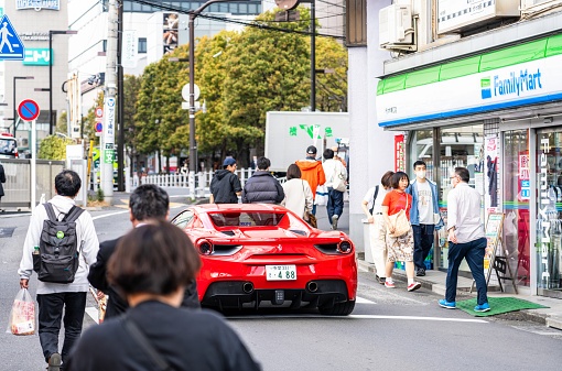 Tokyo, Japan - Rear view of a red Ferrari 488, driving slowly on a local street with pedestrians on the street and sidewalk.