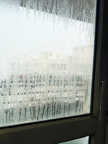 Stock photo showing close-up view of condensation on steamed up  glazed window pane in door with white painted wooden frame.