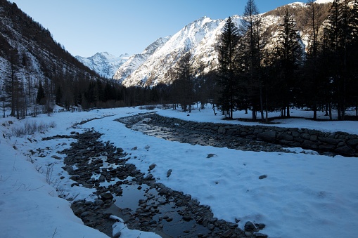 The Gran Paradiso mountain range rises at the head of the Valnontey valley, furrowed by its stream. It is winter; the sunlight is dim.