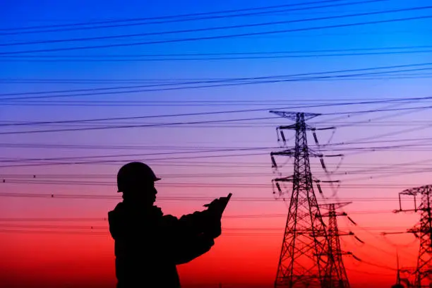 Photo of worker and electric power tower silhouette