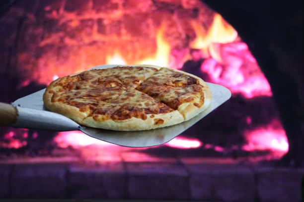 istock Image of cooked Pizza Margherita on long handled pizza paddle, removed from stone base pizza oven, burning wood and flames background, focus on foreground 1886951598