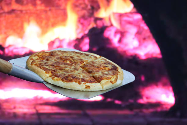istock Image of cooked Pizza Margherita on long handled pizza paddle, removed from stone base pizza oven, burning wood and flames background, focus on foreground 1886952117