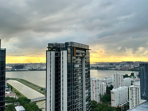 HDB and condominium on the shore of the bay in downtown district. Raining season in Singapore, cloudy sky, sunset. A seaport in the distance