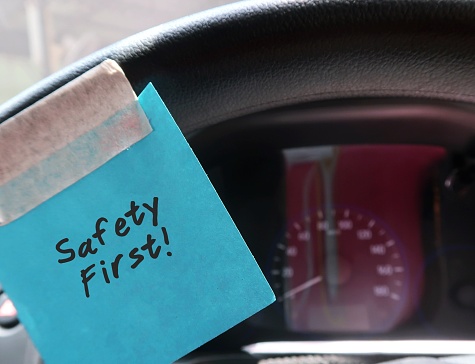 A blue paper note sticking on the car steering wheel, with text written SAFETY FIRST, to remind the driver to drive carefully on the road.
