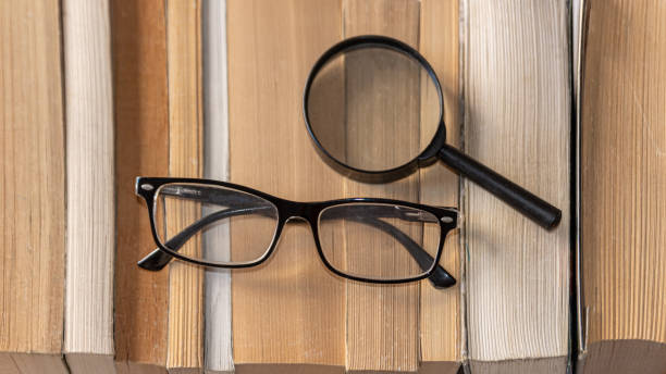 istock Black glasses for reading with magnifying glass on books background 1886995429