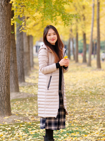 Portrait of Chinese girl in Long down jacket enjoy carefree time in forest park in sunny day. Winter outdoor fashion portrait of glamour young Chinese lady beautiful stylish woman, female lifestyle.