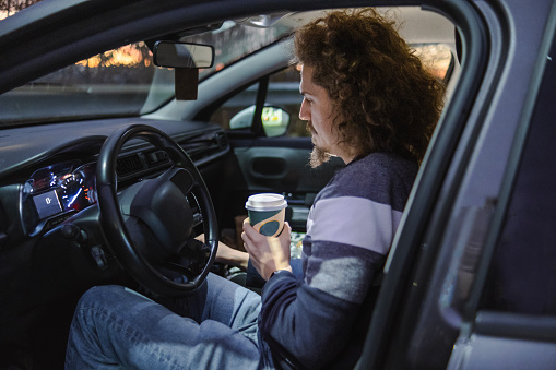 One young man sitting in his car and drinking coffee before work