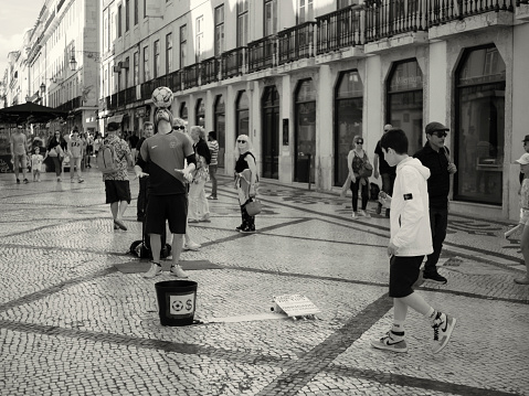 Lisbon, Portugal - June 10, 2023: A street artist perfoms a juggling act with a soccer ball at the Rua Augusta street in Lisbon downtown.
