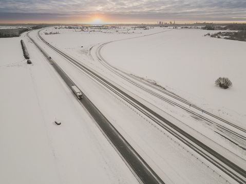 A highway exiting the city of Tallinn in winter, a truck and other vehicles drive along the road, photo from a drone at dawn. High quality photo