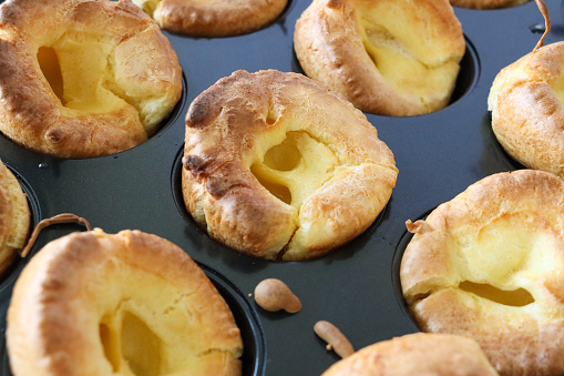 Stock photo showing close-up, elevated view of a tray of individual Yorkshire puddings cooked to be served with a roast dinner. These freshly baked Yorkshire puddings have risen especially well, due to preheating the tray and adding extra eggs to the batter.