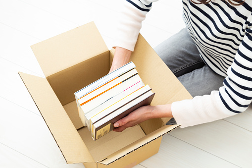 A woman puts unnecessary books into boxes.