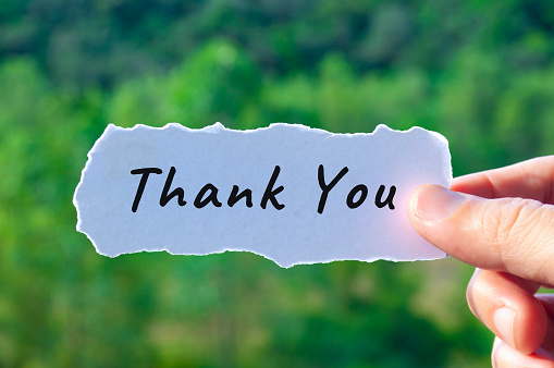 Thank you text on torn white paper with nature background.
