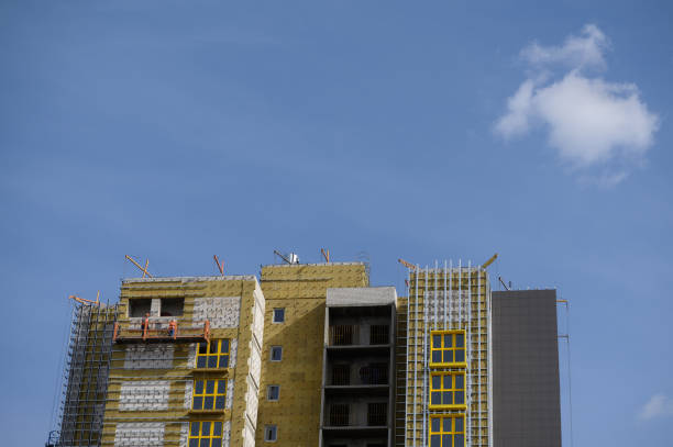 los trabajadores recubren las paredes exteriores del edificio con aislamiento. aislamiento de la fachada del edificio. acabado exterior - recubrimiento capa exterior fotografías e imágenes de stock