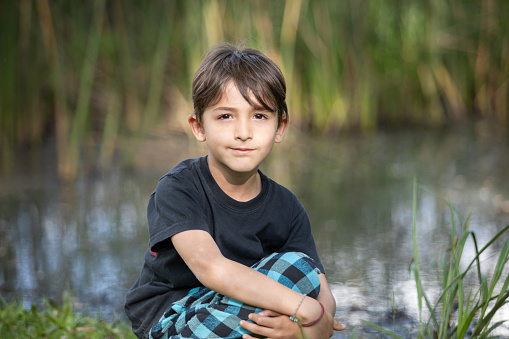 Happy boy child is smiling enjoying adopted life. Portrait of young boy in nature, park or outdoors. Concept of happy family or successful adoption or parenting. The concept of outdoor recreation, vacations, childhood, summer, happiness, rest from study.