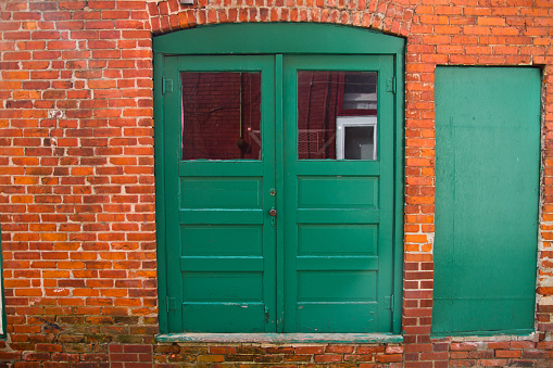 Resilient Vintage Charm: Vibrant green double doors set amidst weathered red brick wall in Allegan, Michigan urban alleyway.