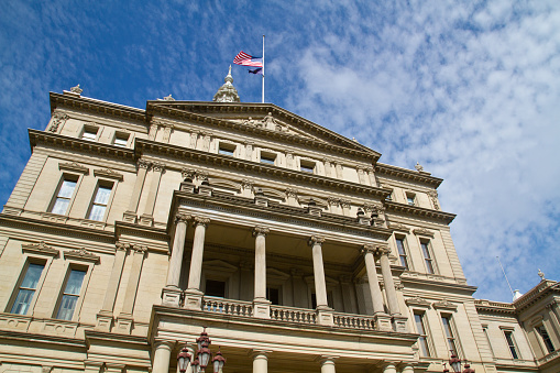 Iconic Government Building in Lansing, Michigan: A majestic symbol of authority and governance, this stately classical structure showcases intricate detailing, ornate columns, and decorative sculptures. With the American and state flags.