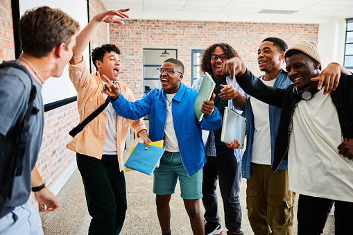 Ecstatic group of diverse young male college students chanting and dancing in a huddle in a school hallway