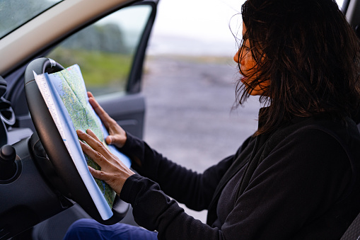 Woman looking at a map on the steering wheel of her open car giving the feeling of being lost