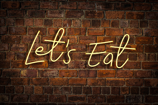 A Vibrant Yellow Neon Sign Saying Let's Eat In A Restaurant Or Cafe