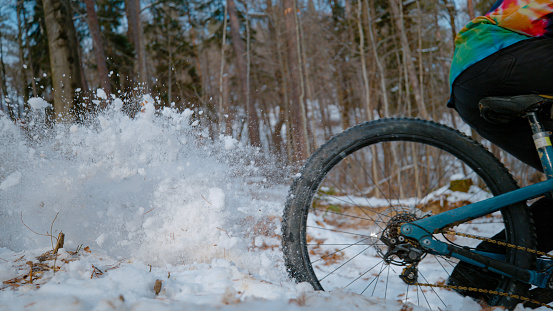 CLOSE UP: Mountain biker sprays snow while riding corner at snowy forest trail. Action bike ride in the woods after fresh snowfall. Spice of adrenaline during mountain biking in winter conditions.