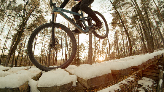 CLOSE UP: Bike rider doing wheelie in beautiful golden light on snowy trail. Fun and adrenaline-filled bike ride through the woodlands. Action mountain bike riding in the woods after fresh snowfall.