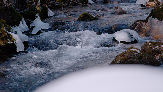 CLOSE UP: Wild mountain river winding and cascading between snowy and icy rocks. Alpine creek with small white rapids on a cold winter day. Beautiful view of crystal clear and free flowing water.