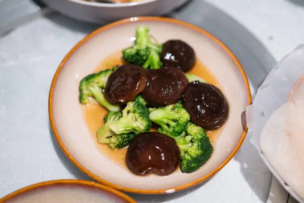 Shiitake mushroom mixed broccoli vegetable stir-fired with oyster sauce, Chinese food menu that served in ceramic dish. Food object photo, close-up.