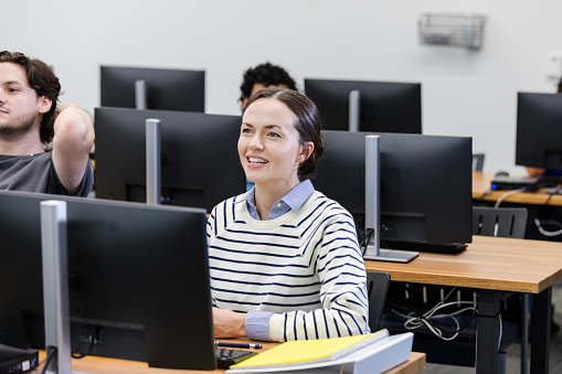 A young adult woman interacts with an unseen professor during a class in the university computer lab.