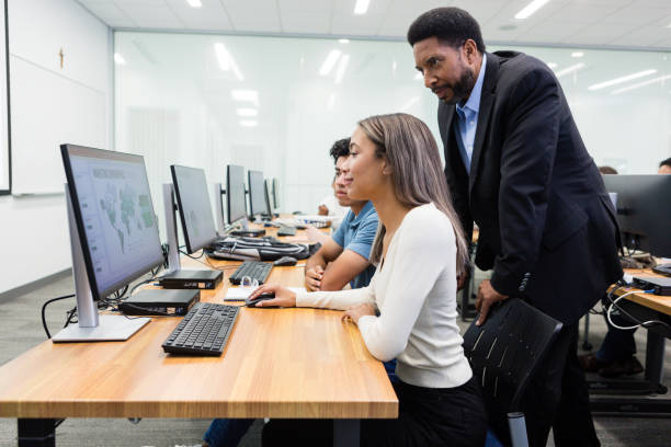 istock Male professor looks at computer graphic over students' shoulders 1887375715