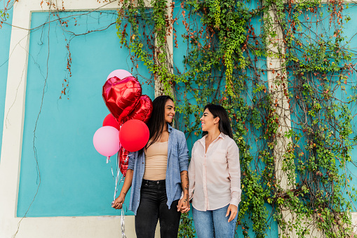 Lesbian couple holding red balloons heart celebrating valentine's day in the city