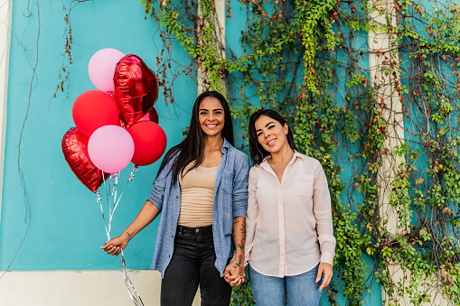 Portrait of a lesbian couple holding red balloons heart celebrating valentine's day in the city