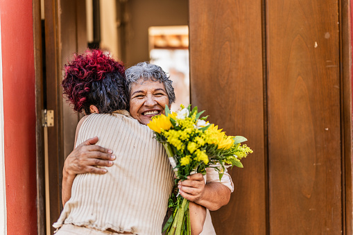 Grandmother embracing her granddaughter after receiving a bouquet of flowers at home