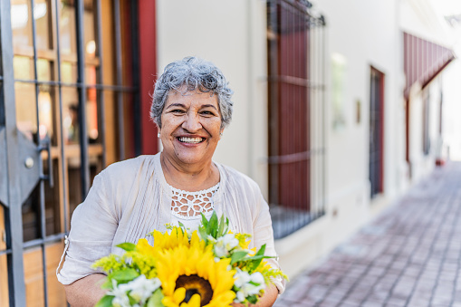 Portrait of a senior woman holding a bunch of flowers in the city