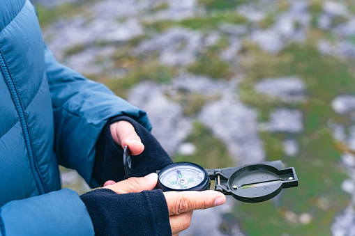 Close up of hands protected from the cold taking a compass in a stone landscape in Ireland