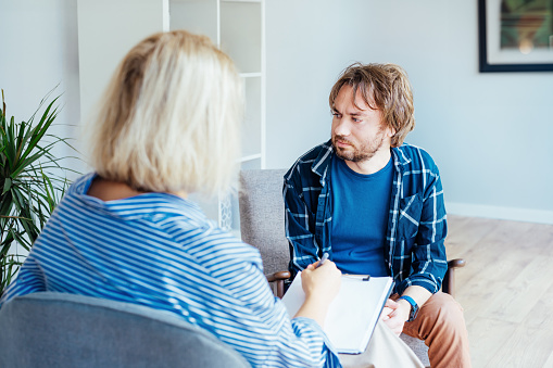 Depressed male patient having psychotherapy session with counselor at mental health clinic. Man with emotional problems consulting professional therapist i comfy office. Psychological help service