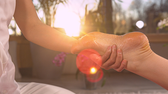 CLOSE UP: Sun shinning through massaging hands while performing reflexotherapy. Reflexology therapy for stress ease and helping body work better. Relaxing wellness treatment at the end of the day.