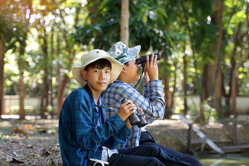 Asian boys use binoculars to look at birds in a community forest own. The concept of learning from learning sources outside the school. Focus on the first child.