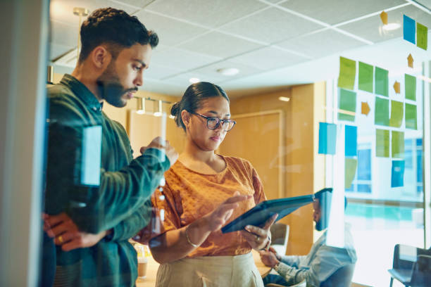 istock Two colleagues discussing ideas in front of a glass wall with sticky notes. 1887444233