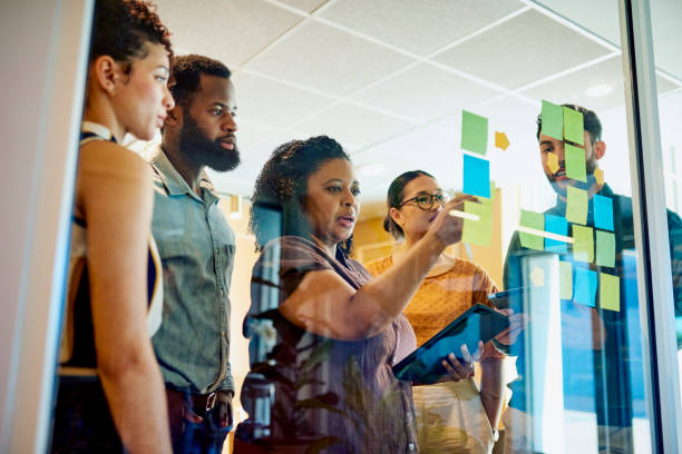 diverse professionals brainstorming on a glass wall with sticky notes - werkplek stockfoto's en -beelden