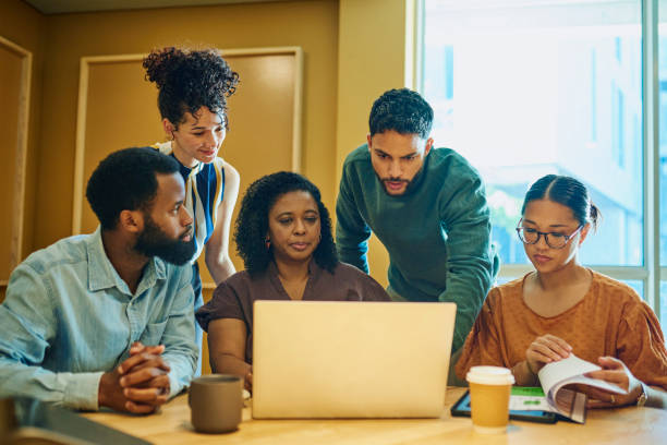 Diverse Business Professionals Collaborating on Laptop Project A group of diverse business professionals gathered around a laptop, discussing and working on a project together. research ethics stock pictures, royalty-free photos & images