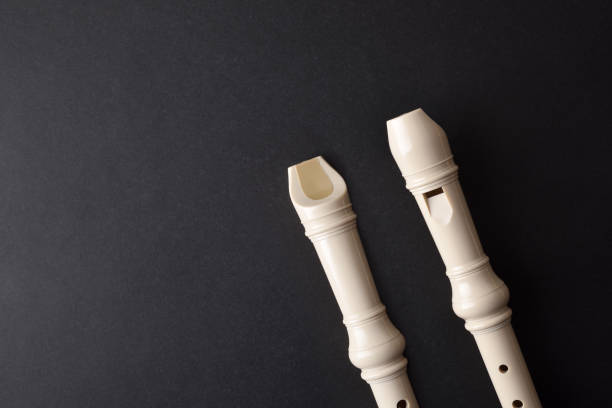 Top and bottom view of two white plastic recorder mouthpiece in diagonal position on black textured table. Top view.