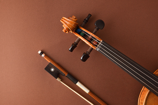 Detail of peg box and fingerboard of traditional stringed violin and bow on isolated gradient brown background.. Top view.