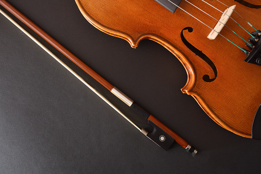Traditional stringed violin and bow placed diagonally on isolated gradient black background. Top view.