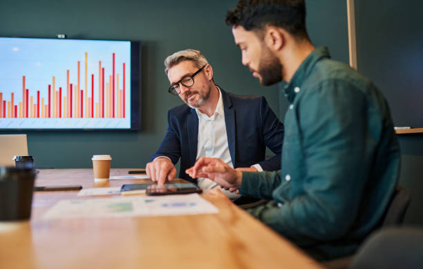 istock Two businessmen in suits sit at a conference table and review financial data on a tablet. 1887449058